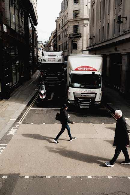 The image shows a light grey moving van parked on a narrow urban street in Whitechapel, with the rear doors open and a man with a white shirt and dark trousers loading or unloading cardboard boxes and