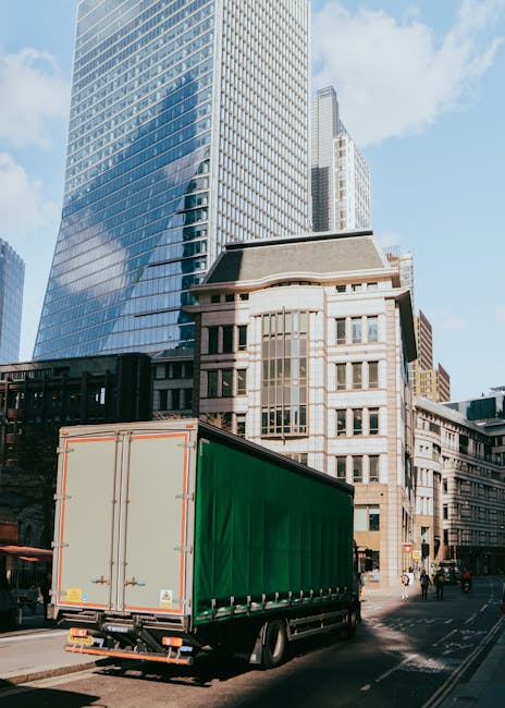 Two white moving vans parked on a curved cobblestone street near a brick wall and an arched bridge in an urban area, with the vans positioned side by side facing in the same direction. The scene appea